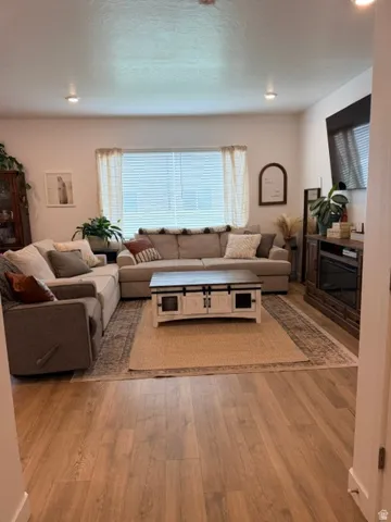 Spacious living area featuring wood-finish flooring, recessed lighting, and a large window with blinds