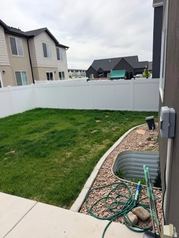 Private backyard featuring a white vinyl fence, established lawn, and a side yard with decorative rock landscaping and a basement window well