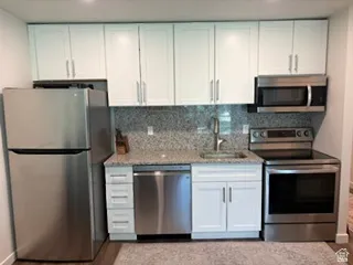 Kitchen featuring white shaker-style cabinetry, stainless steel appliances, granite countertops, and a tile backsplash
