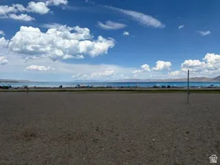 Expansive beach area with a turquoise body of water and distant mountains under a blue sky with white clouds
