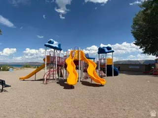 Vibrant playground structure featuring multiple slides, climbing elements, and overhead platforms on a sandy base