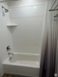 White acrylic bathtub and shower surround with an integrated corner shelf and chrome fixtures