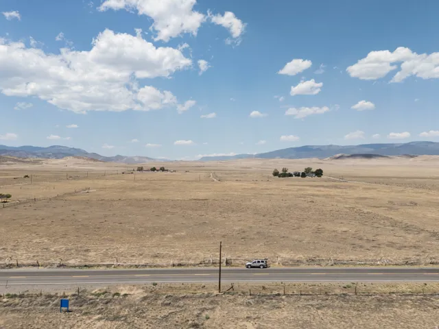Expansive rural property featuring a paved roadway, distant structures, and mature trees, set against a backdrop of rolling hills