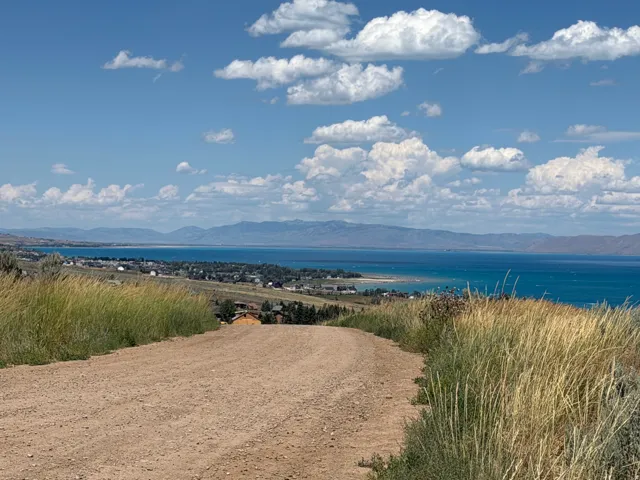 Elevated building site featuring a gravel road, expansive water body, distant mountain range, and scattered residential properties