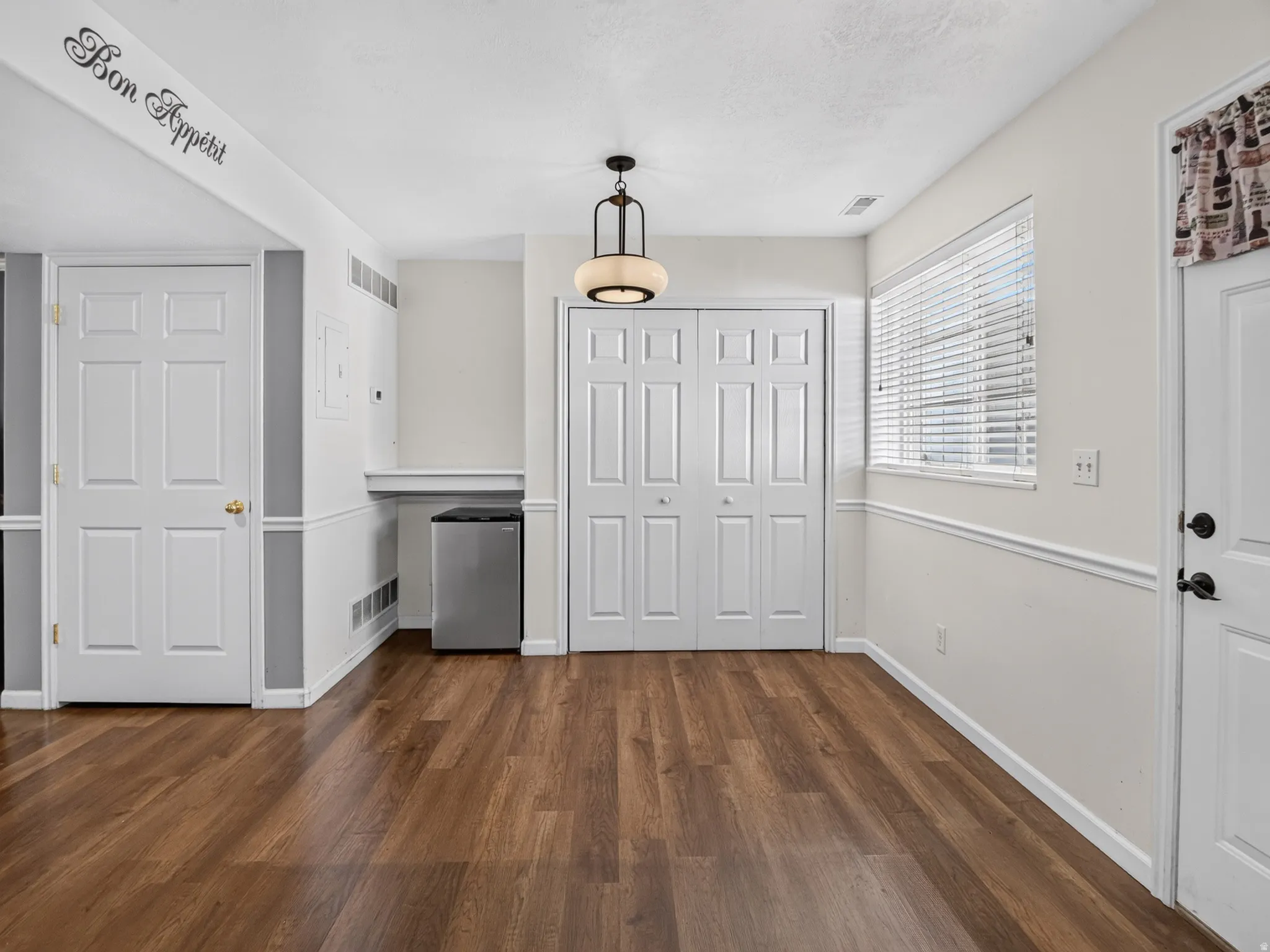 Open area featuring wood-finish flooring, a contemporary ceiling light fixture, and a window with horizontal blinds