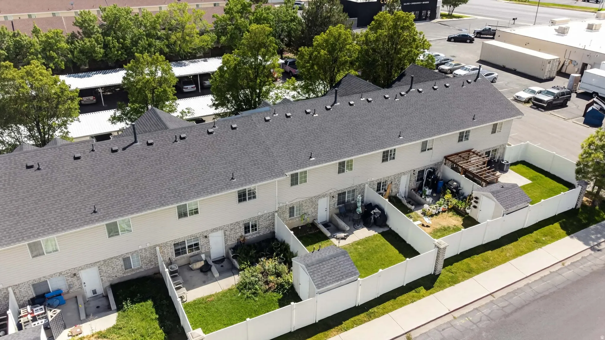 Multi-unit property with private fenced backyards featuring green lawns, individual patios, and detached storage sheds