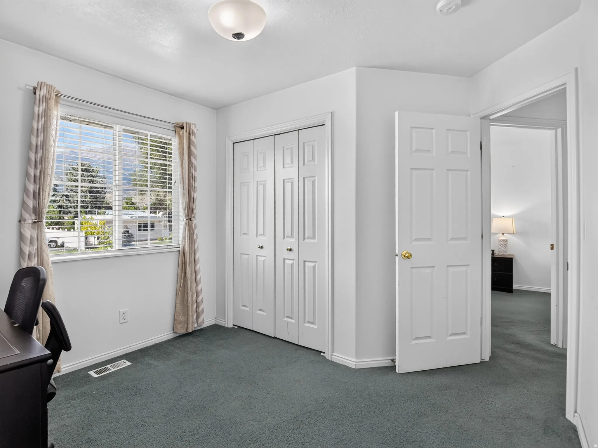 Room featuring an expansive window with blinds, dual bi-fold closet doors, wall-to-wall carpeting, and a flush mount ceiling light