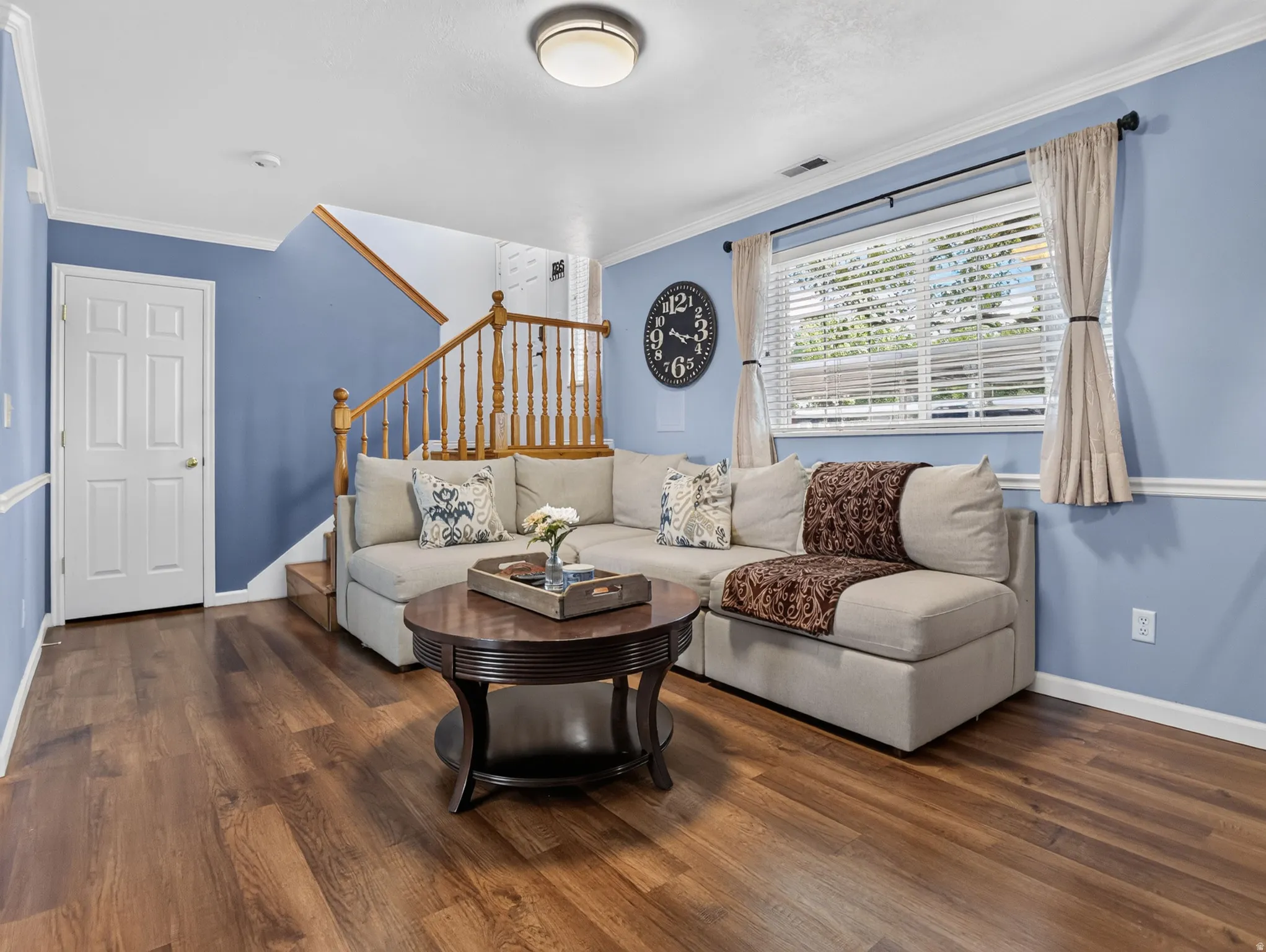 Interior space featuring wood-finish flooring, a white six-panel door, and a staircase with wood newel posts and spindles