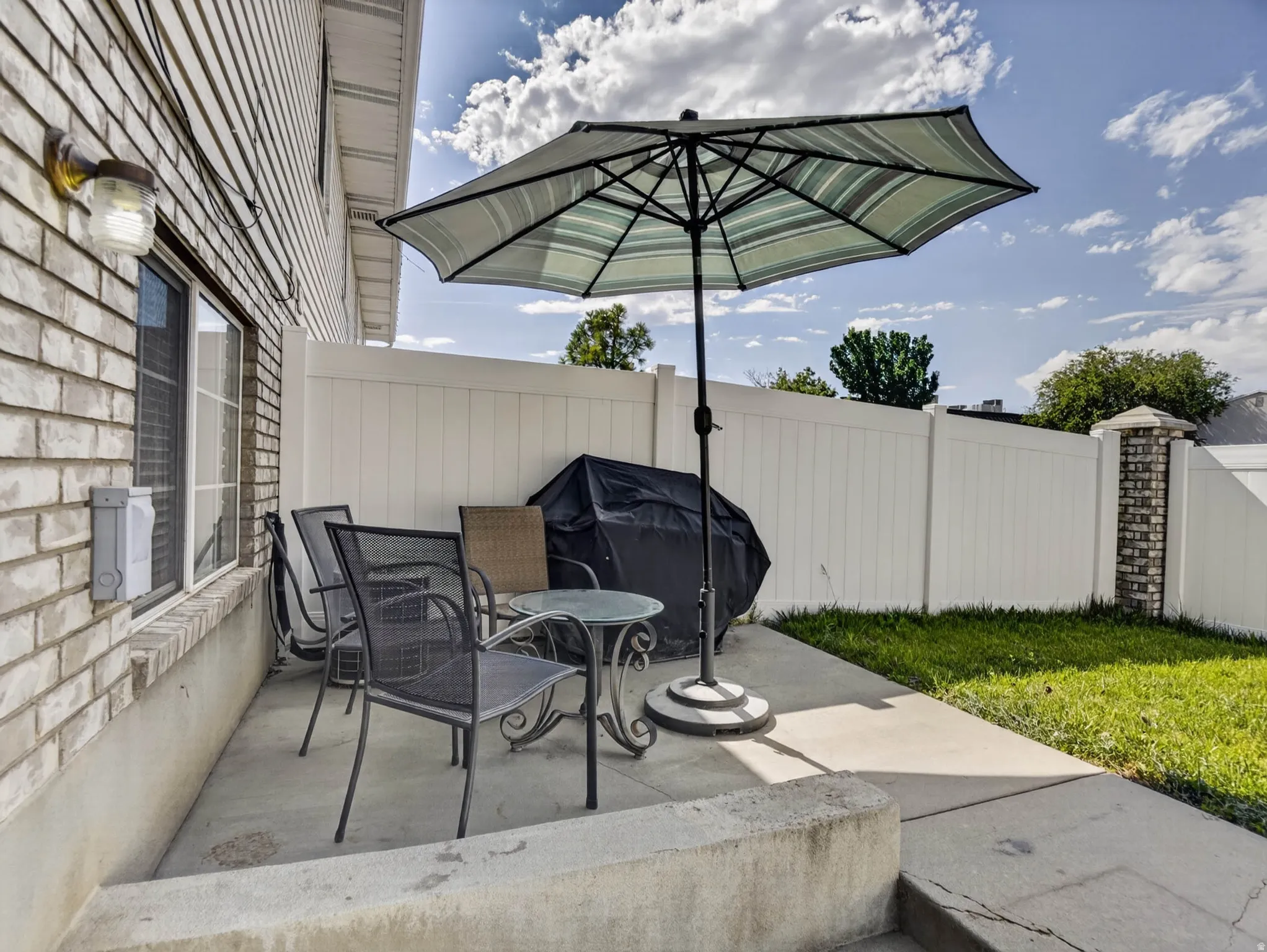 Paved patio area featuring concrete flooring, a white vinyl fence, and brick detailing