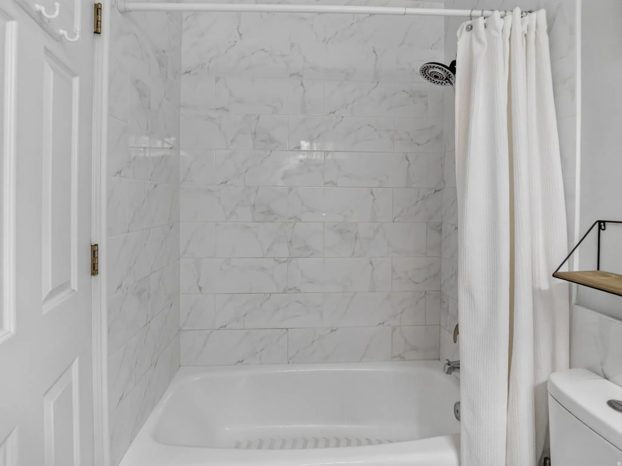 Bathtub and shower combination featuring white subway tile with a subtle marble-like pattern, a fixed showerhead, and chrome fixtures