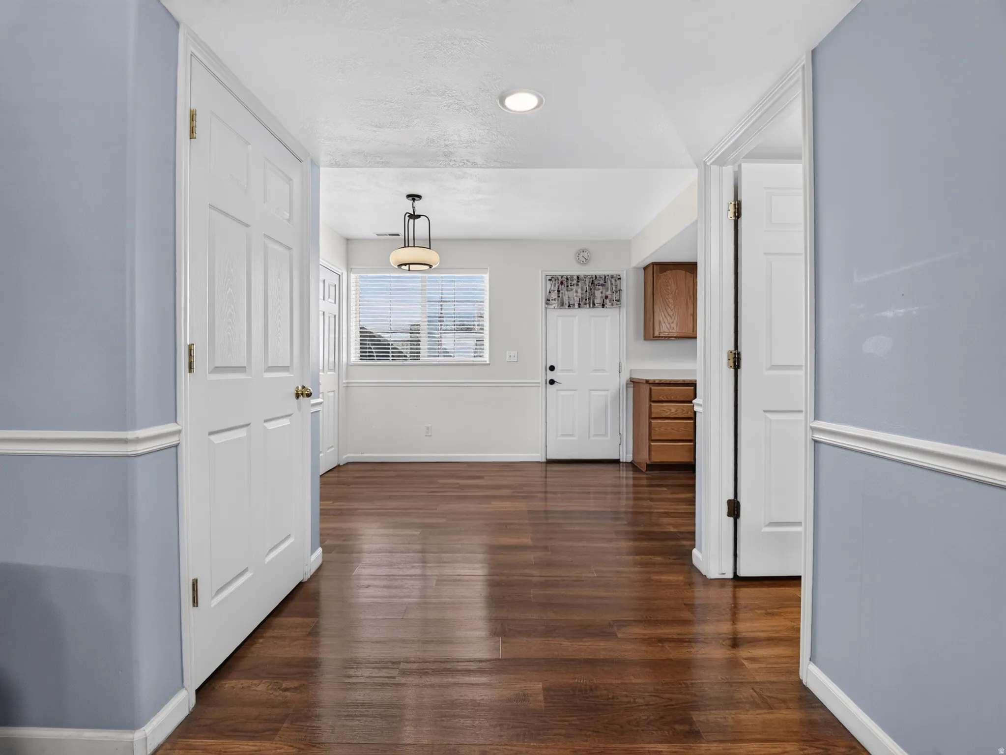Expansive room featuring wood-finish flooring, light blue and white painted walls, and a contemporary ceiling light fixture