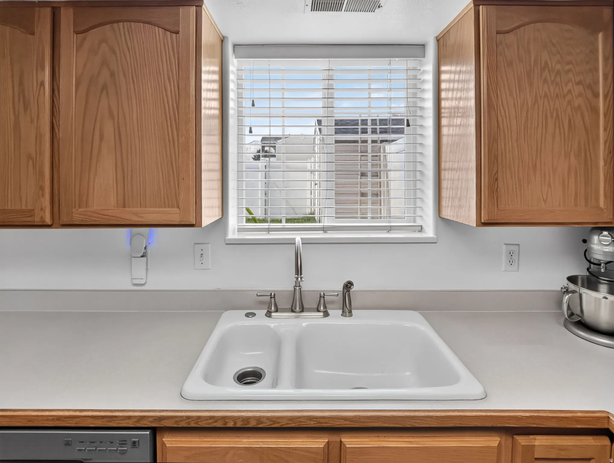 Double-basin sink with a brushed metal faucet, framed by a window with horizontal blinds