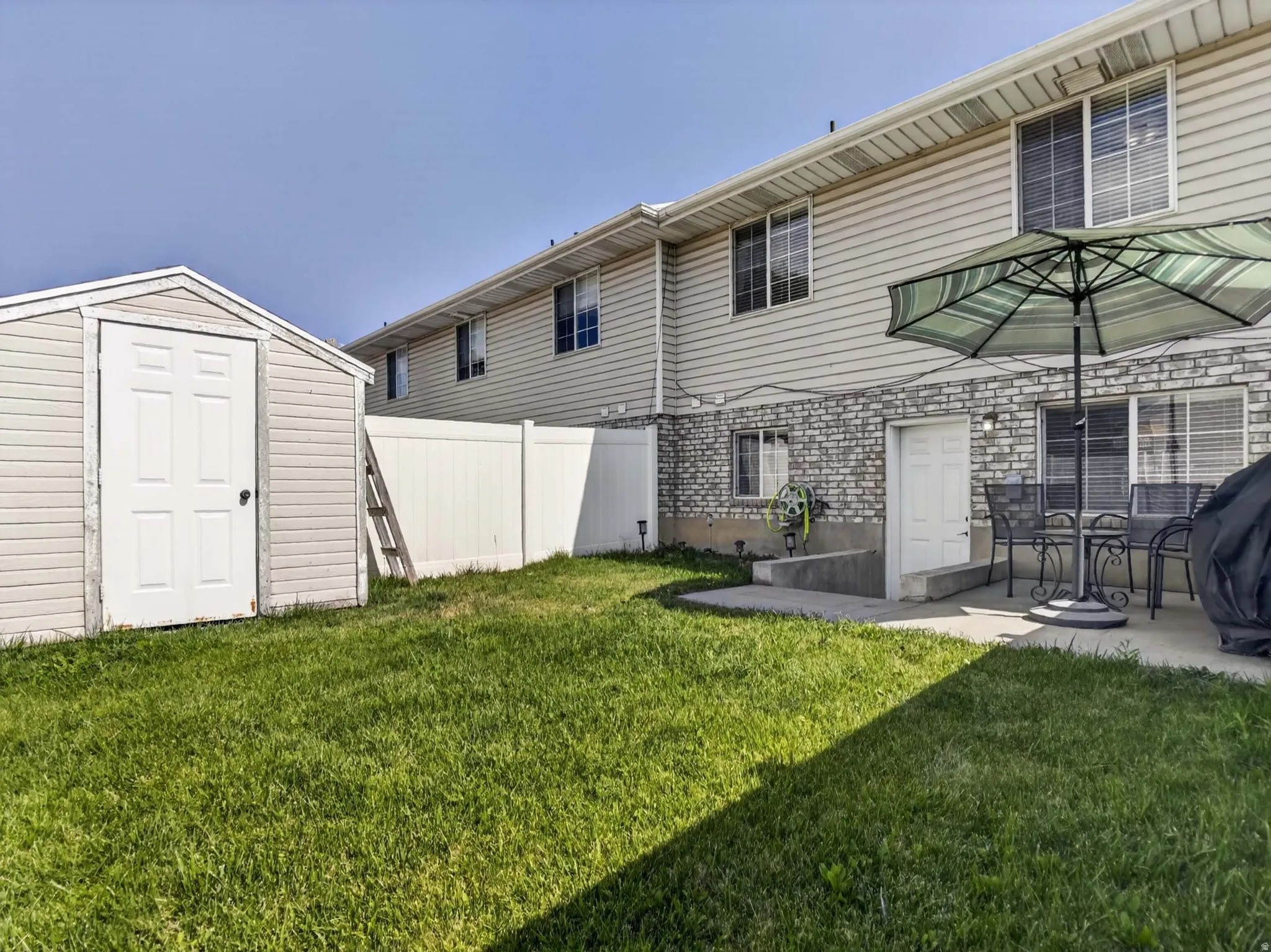Private backyard featuring a storage shed, white vinyl fencing, and a concrete patio