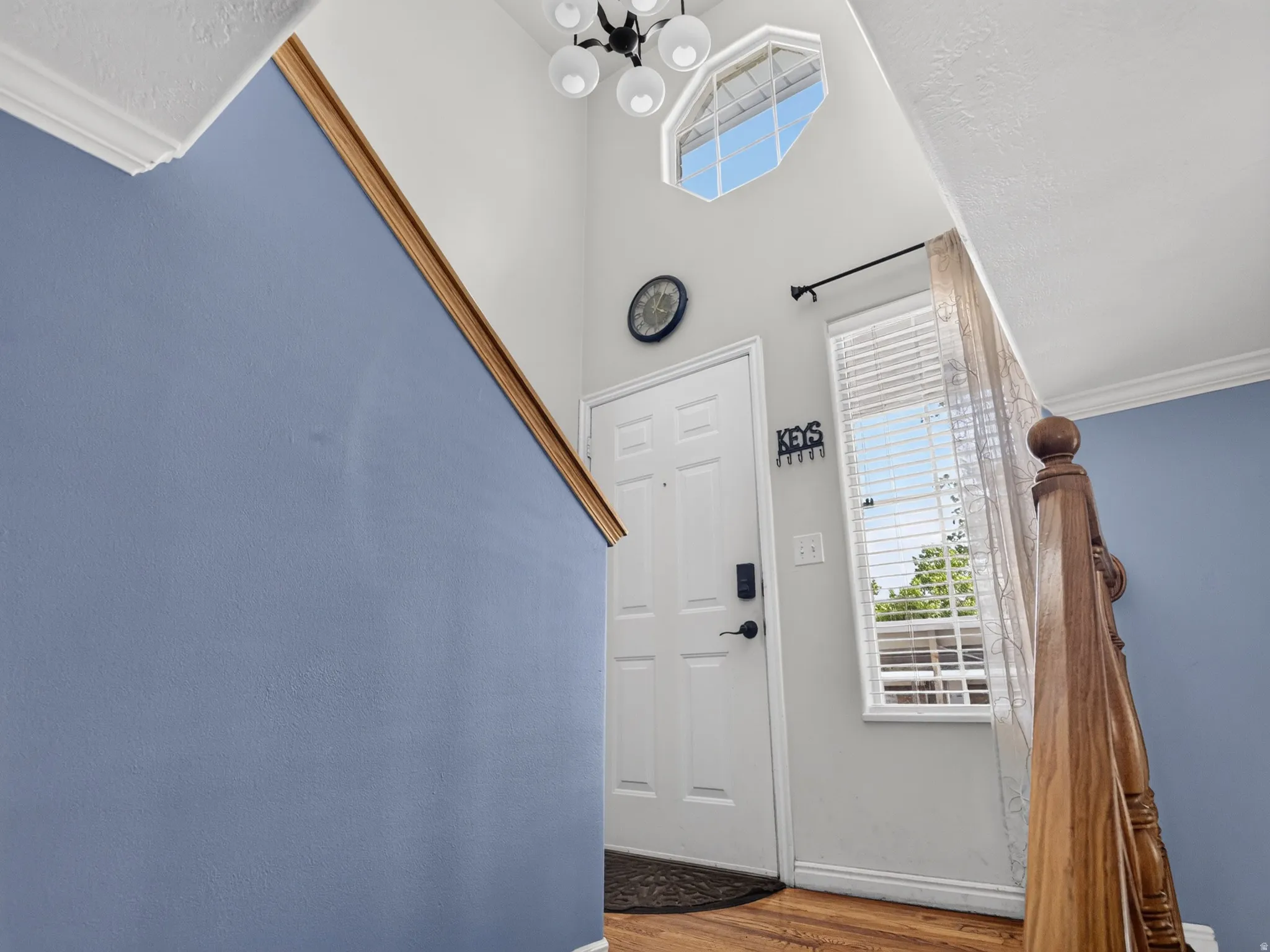 Entryway featuring a white paneled door with smart lock hardware, wood-finish flooring, a decorative octagonal window, and a chandelier-style light fixture