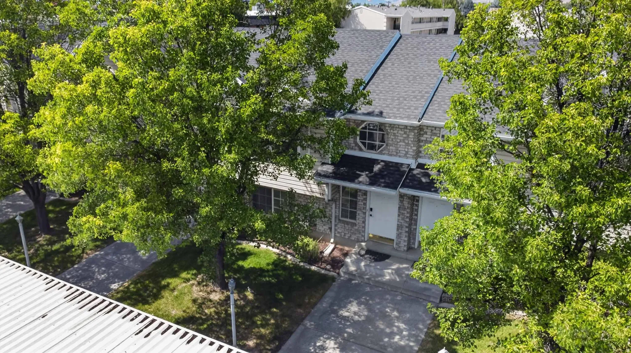 Stone facade residence featuring a prominent circular window, asphalt shingle roof, paved driveway, and mature landscaping