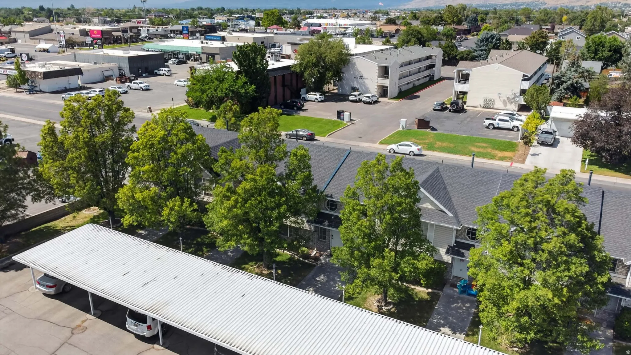 Townhome complex featuring multiple units with dark shingle roofs, mature trees, and a covered parking structure