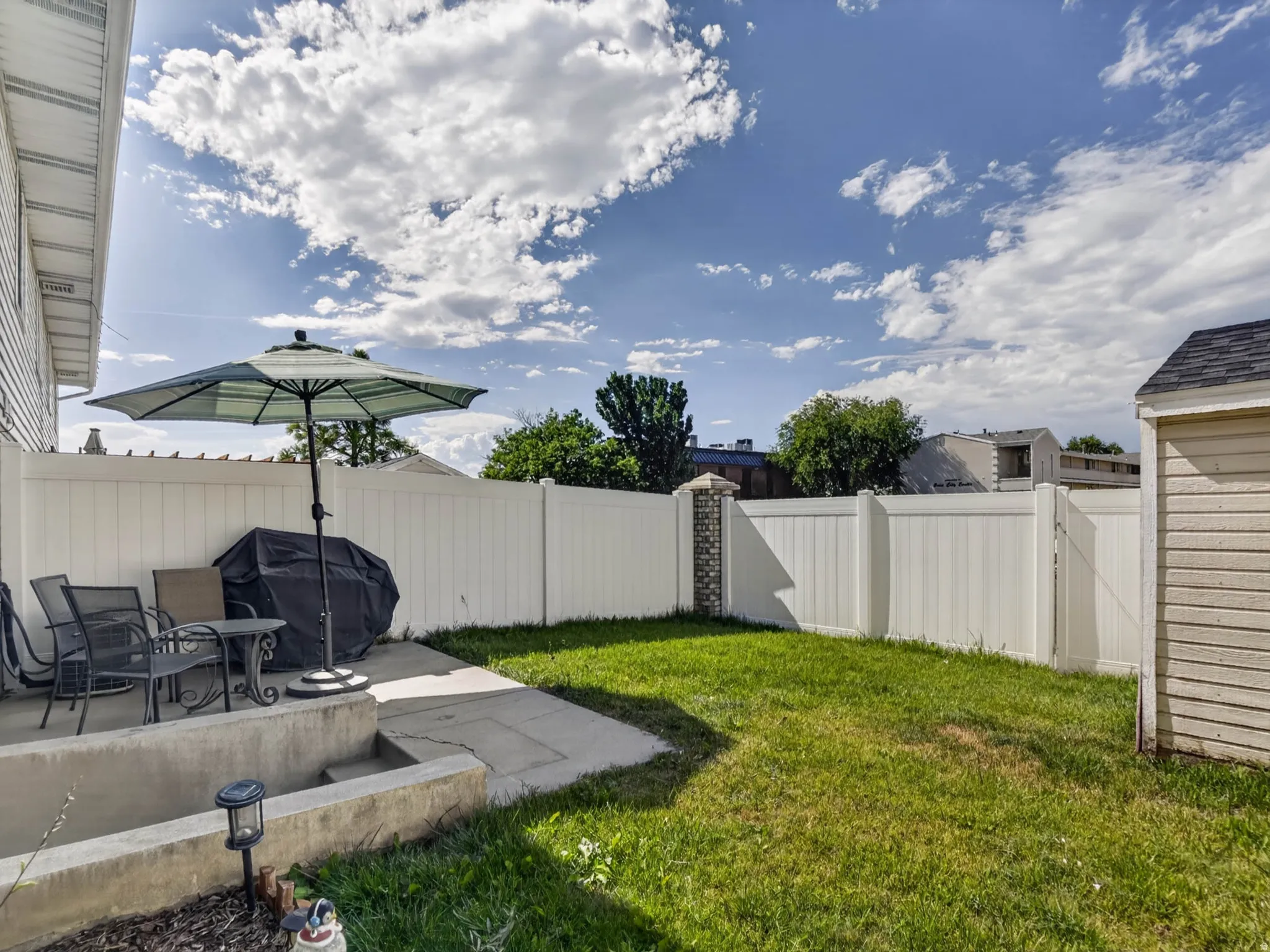 Private backyard featuring a concrete patio, grassy area, and perimeter fencing with a decorative brick column