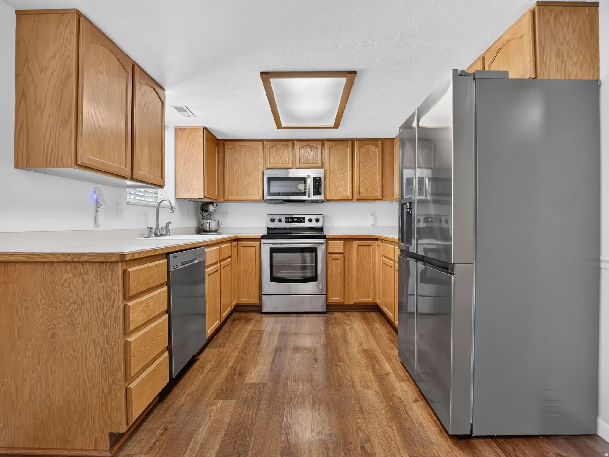 U-shaped kitchen featuring wood-finish cabinetry, light-toned countertops, and wood-finish flooring
