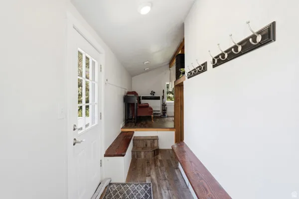 Entryway featuring a paneled glass-insert door, wood-finish flooring, two built-in benches, and wall-mounted coat racks