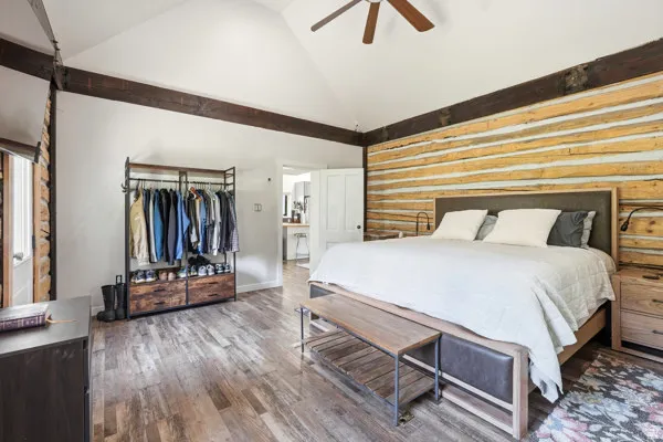 Vaulted ceiling with exposed wood beams, log wall detailing, wood-finish flooring, and a ceiling fan