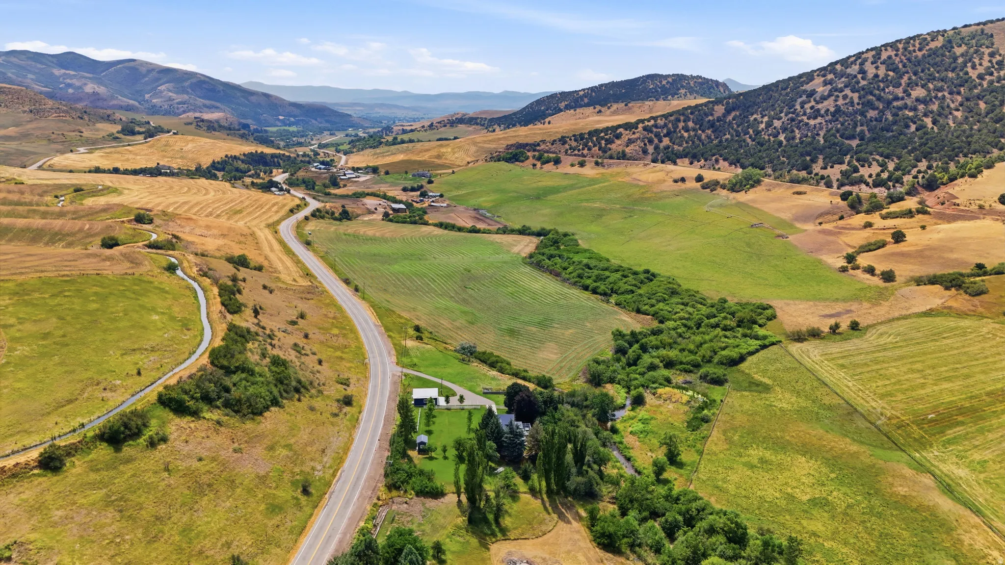 Expansive rural landscape featuring a single-family residence, mature trees, and a paved road