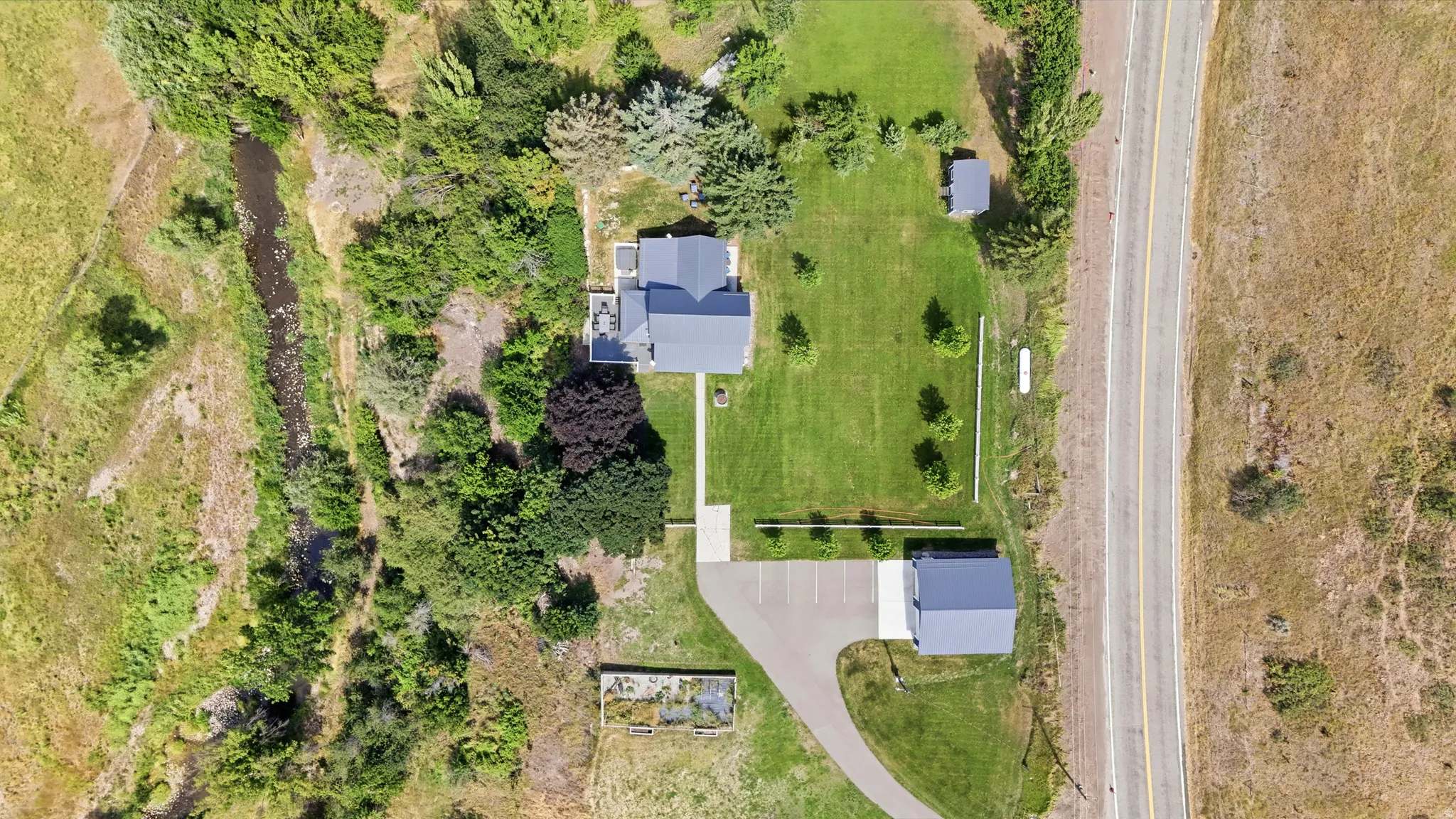 Expansive property featuring a main residence with a gray roof, a detached garage, a secondary outbuilding, and a natural water feature