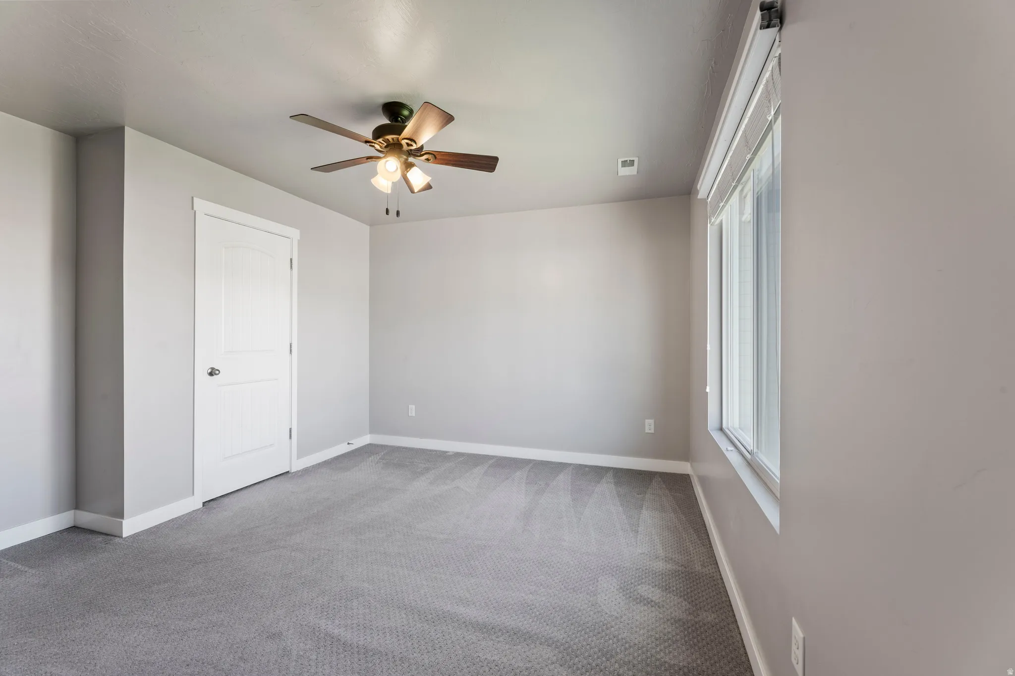 Primary bedroom with a ceiling fan light fixture, a large window, a paneled door, and light gray walls with white trim