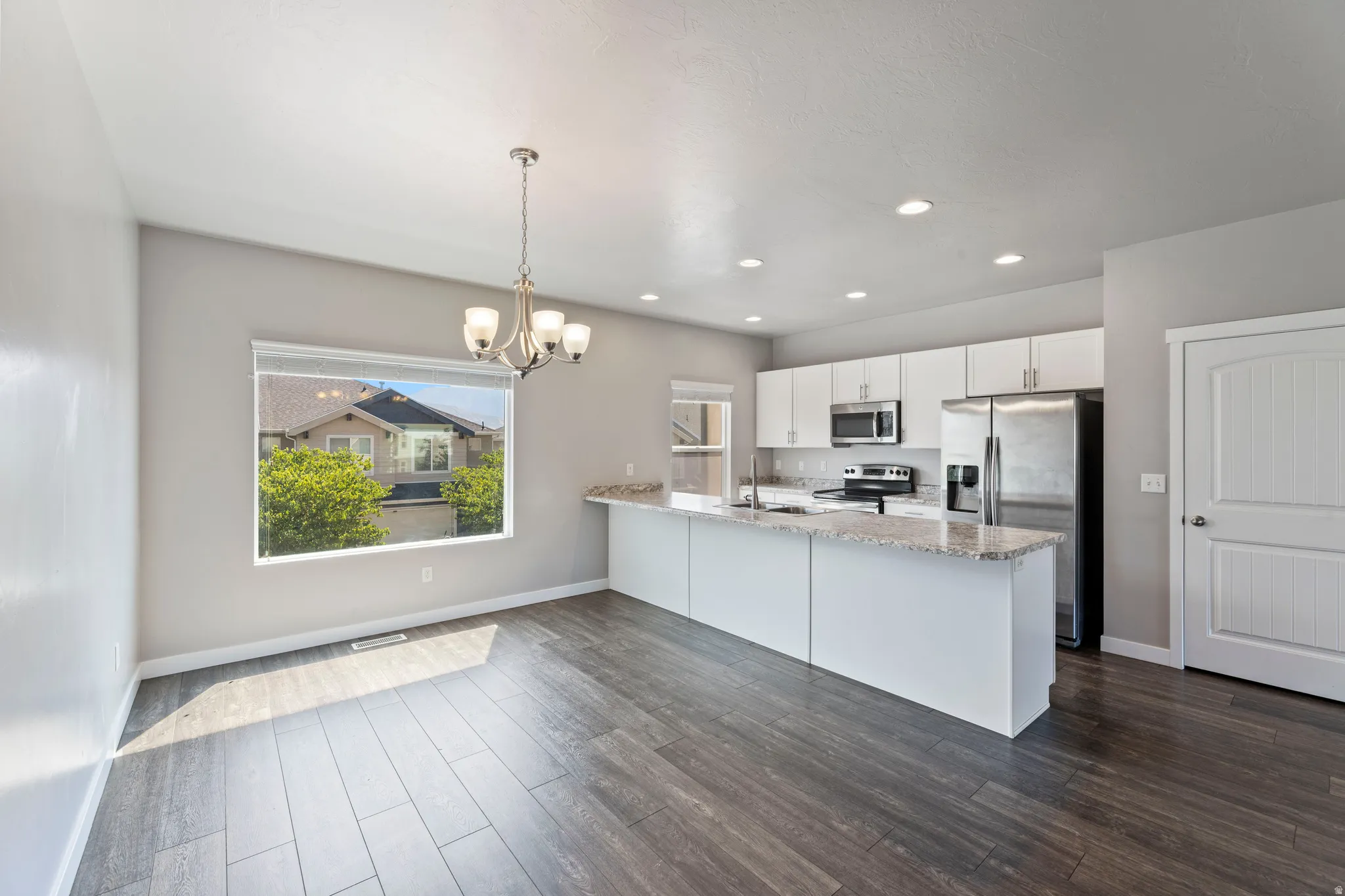 Open-concept kitchen and dining area featuring wood-finish flooring, recessed lighting, and a modern chandelier