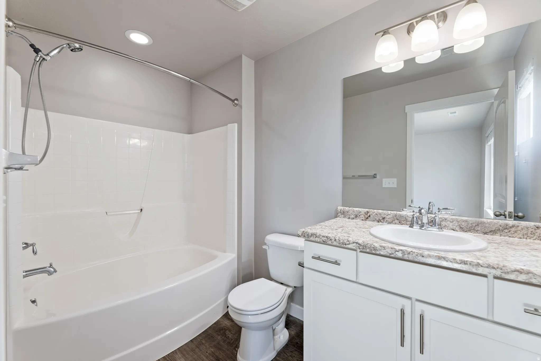Bathroom featuring a white bathtub with an integrated shower, a white vanity with a light-toned countertop, a recessed ceiling light, and wood-finish flooring