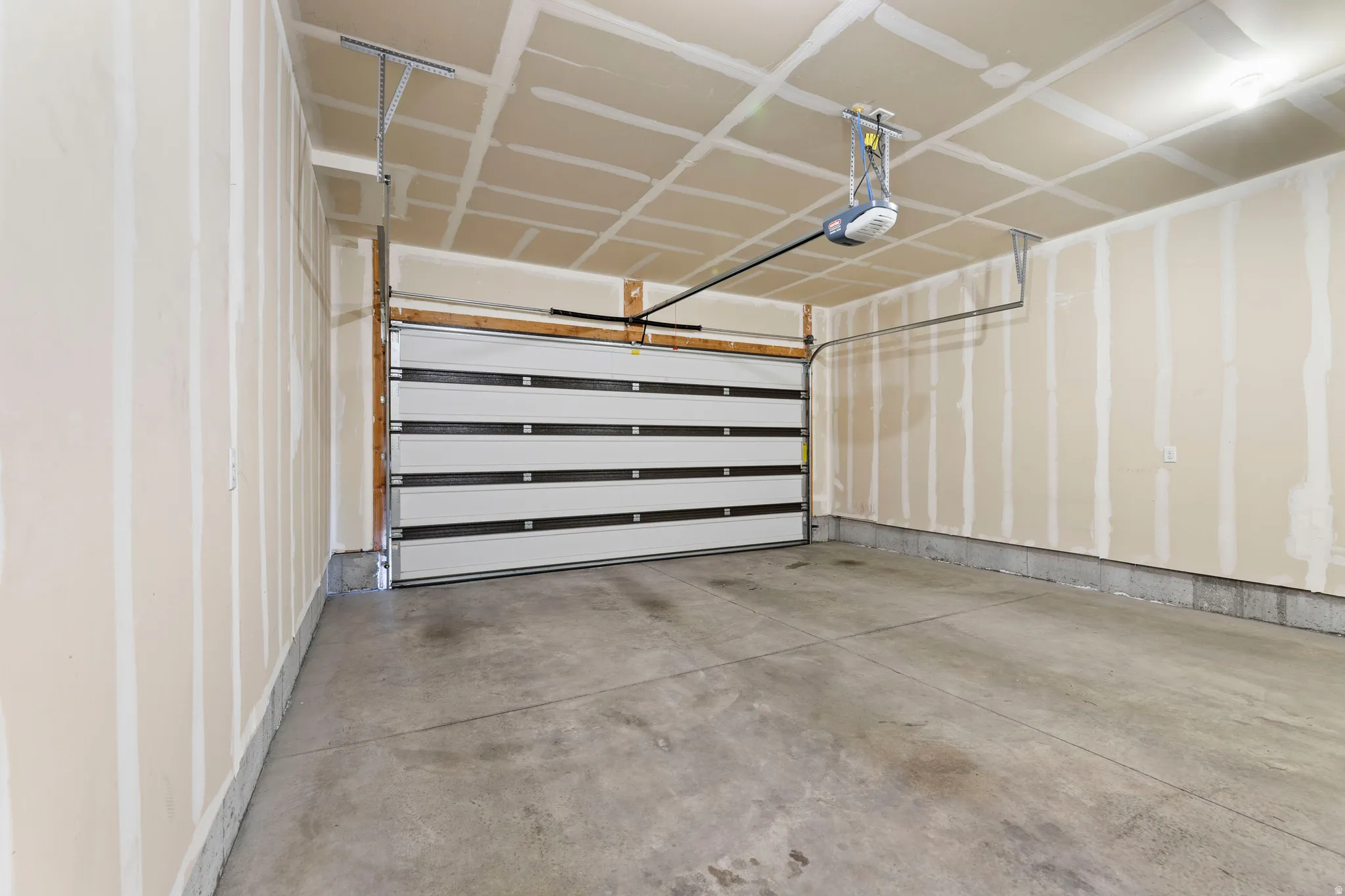 Concrete flooring with a white paneled overhead garage door and an automatic opener
