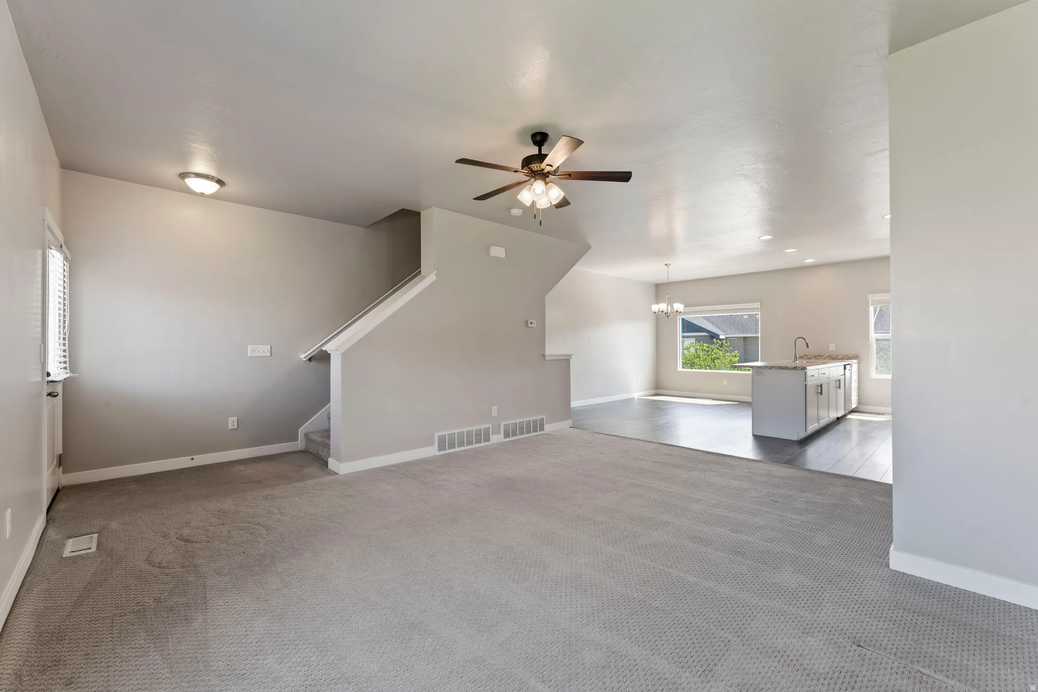 Open-concept living area with light gray carpeting, a ceiling fan, and a staircase