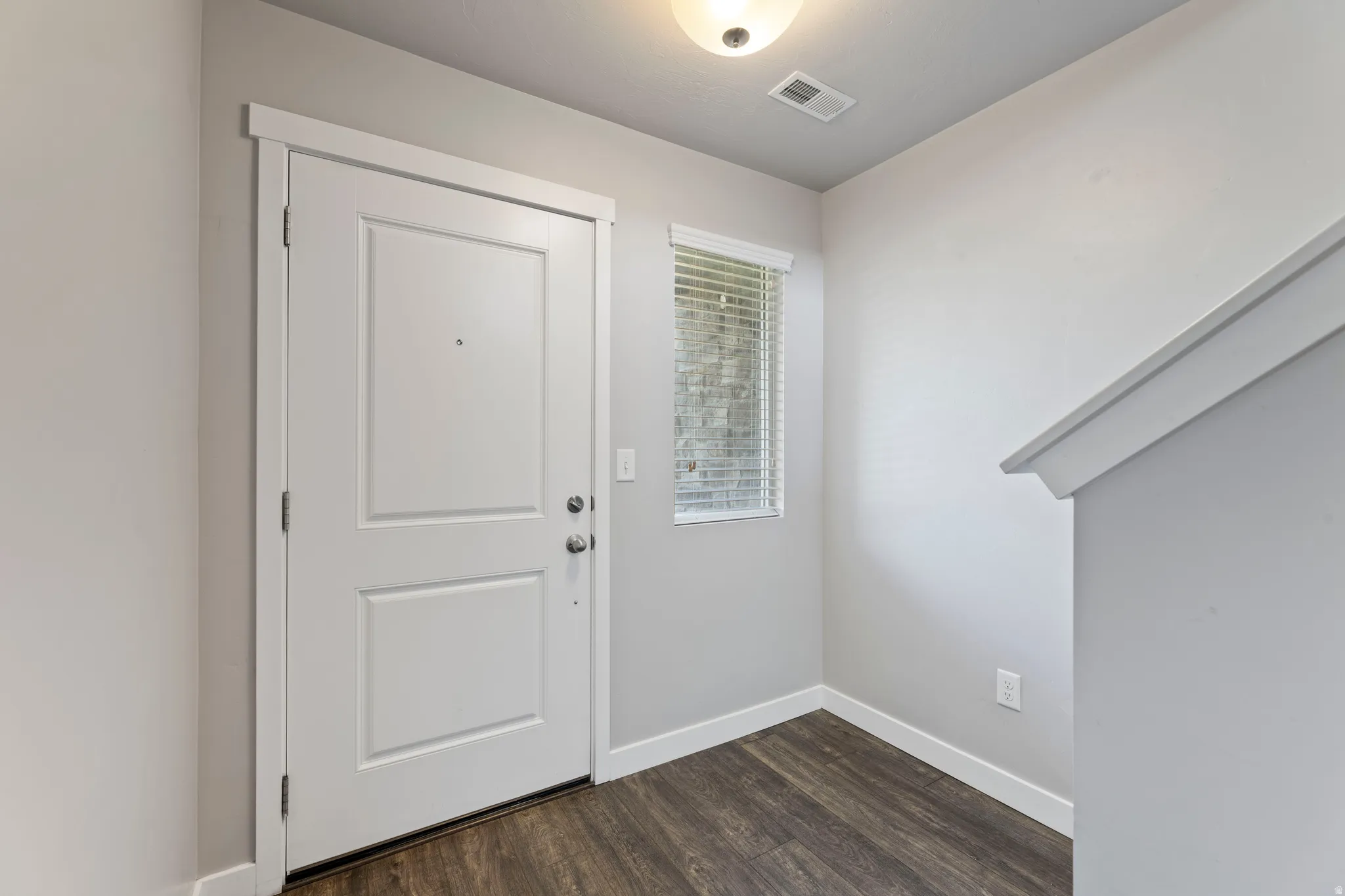 Entryway featuring a white paneled door with brushed nickel hardware, wood-finish flooring, and a window with horizontal blinds