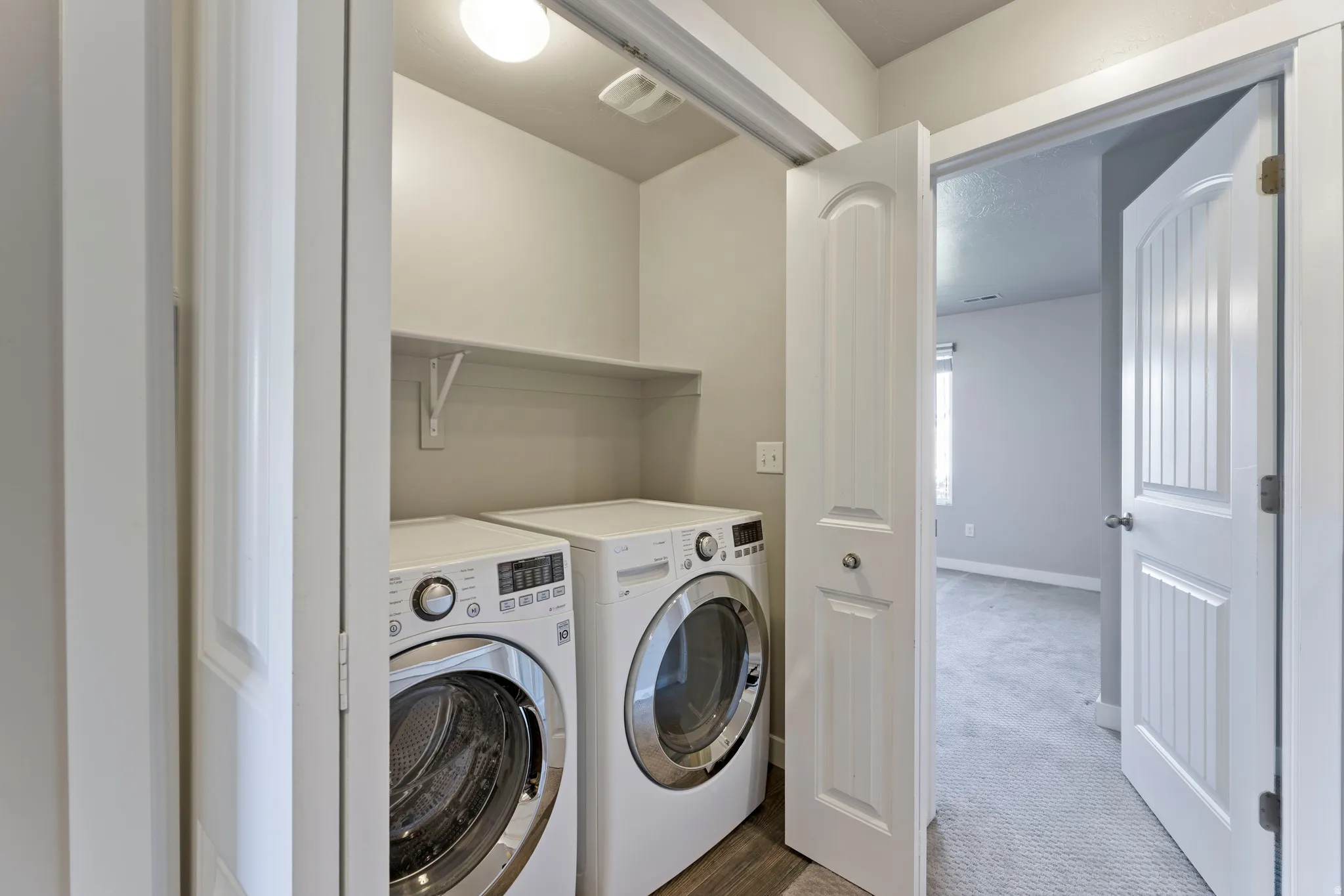 Dedicated laundry closet featuring a built-in shelf, overhead lighting, and wood-finish flooring