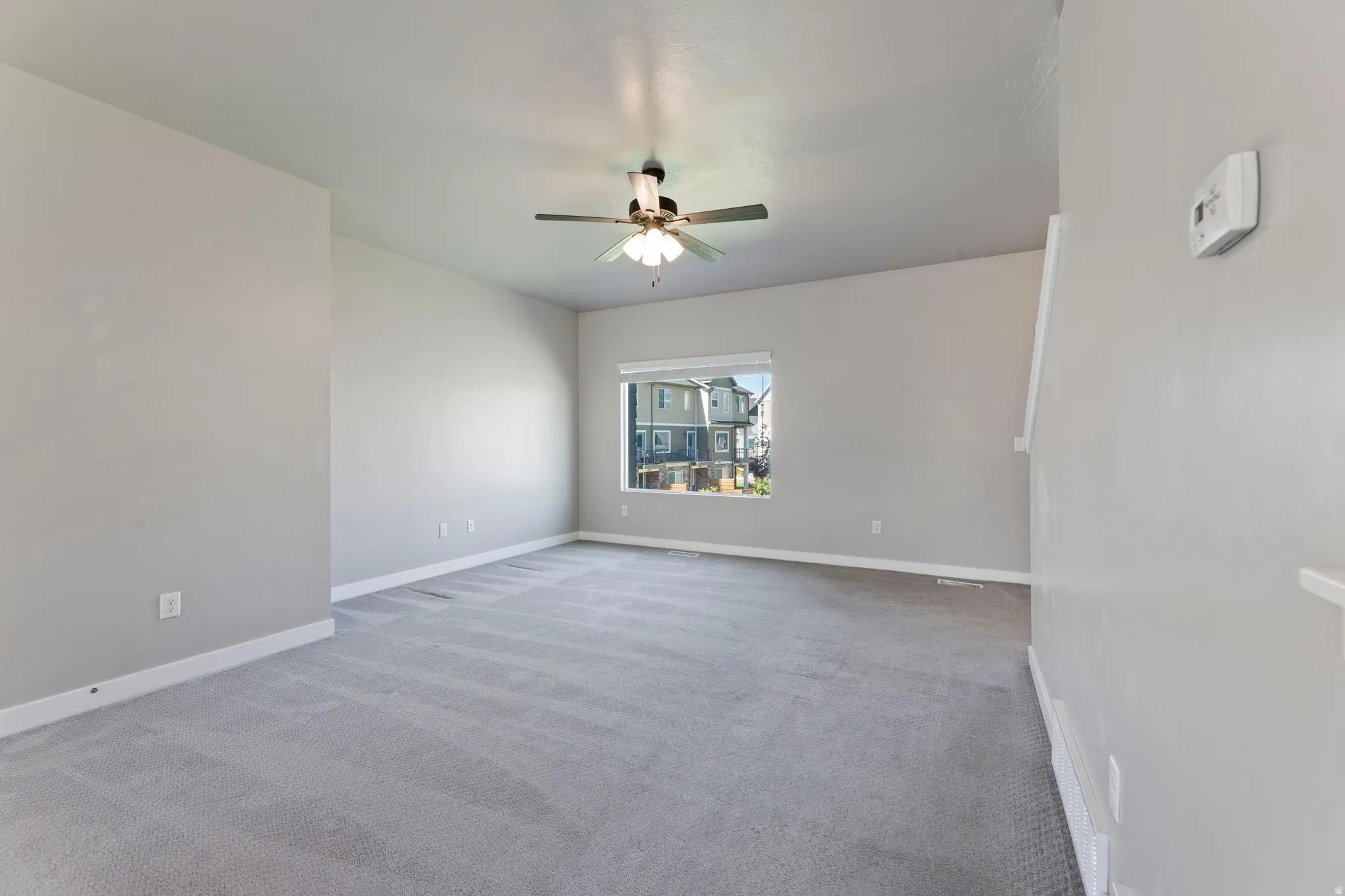 Spacious room featuring light gray carpeting, neutral wall finishes, and a ceiling fan with integrated lighting