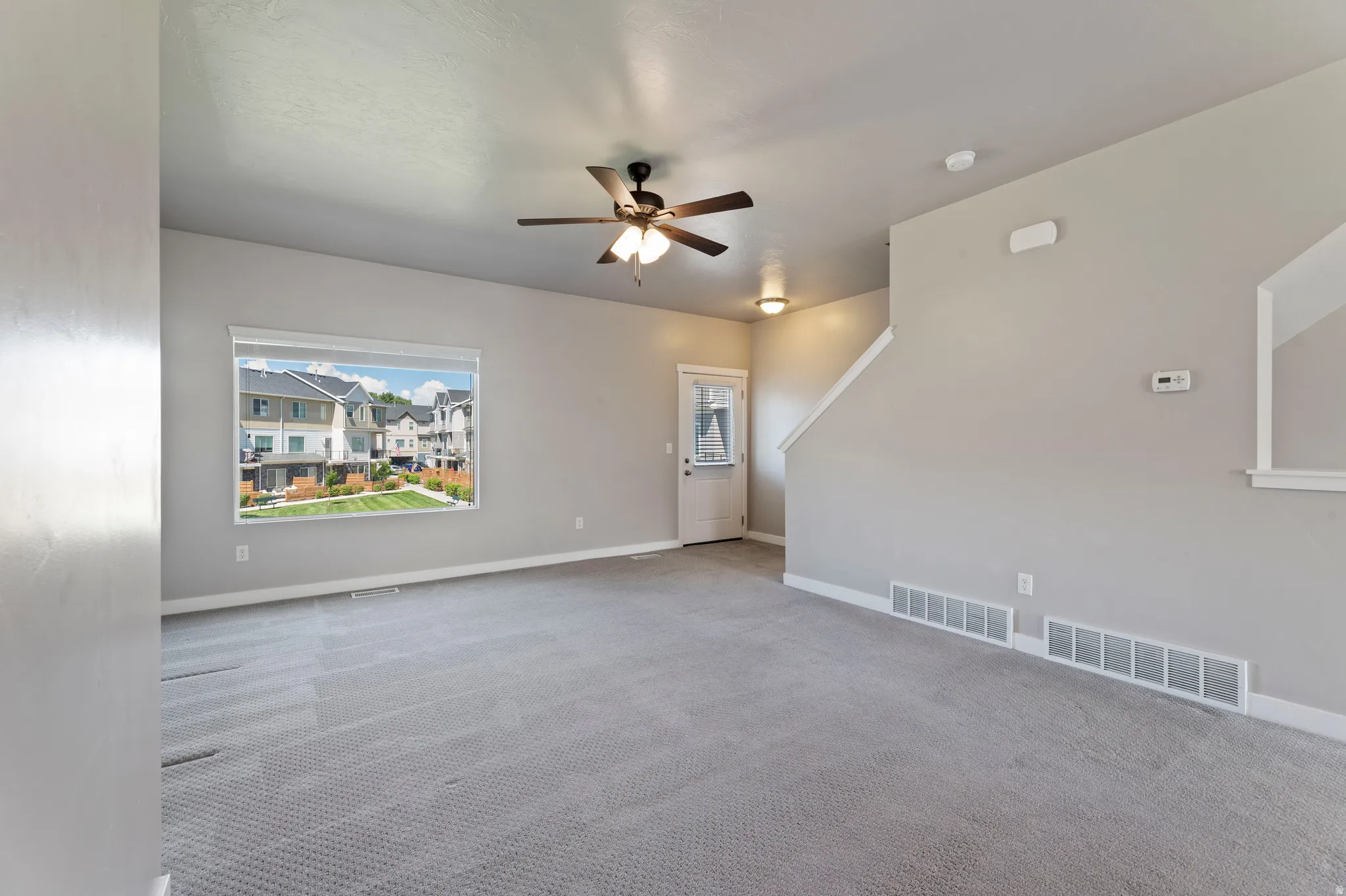 Spacious living area featuring neutral-toned walls, textured gray carpet, and a large window