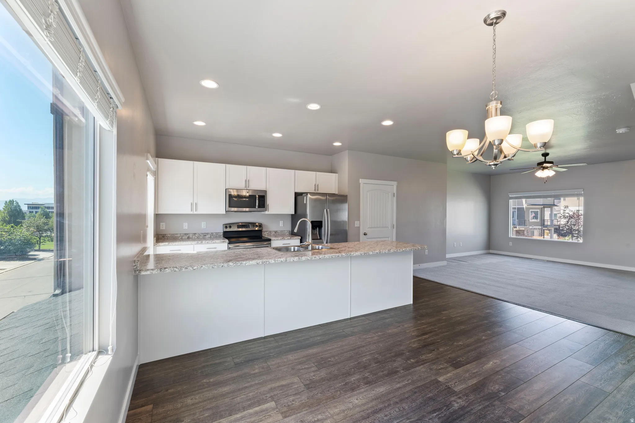 Open-concept living space featuring a kitchen with white cabinetry, stainless steel appliances, and a light-toned countertop