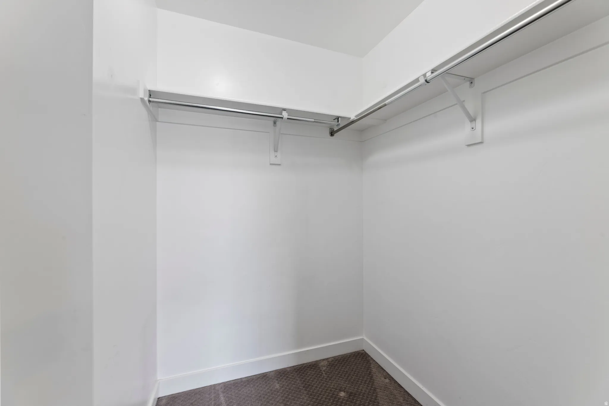 Walk-in closet featuring white walls, white baseboards, and a dark carpeted floor