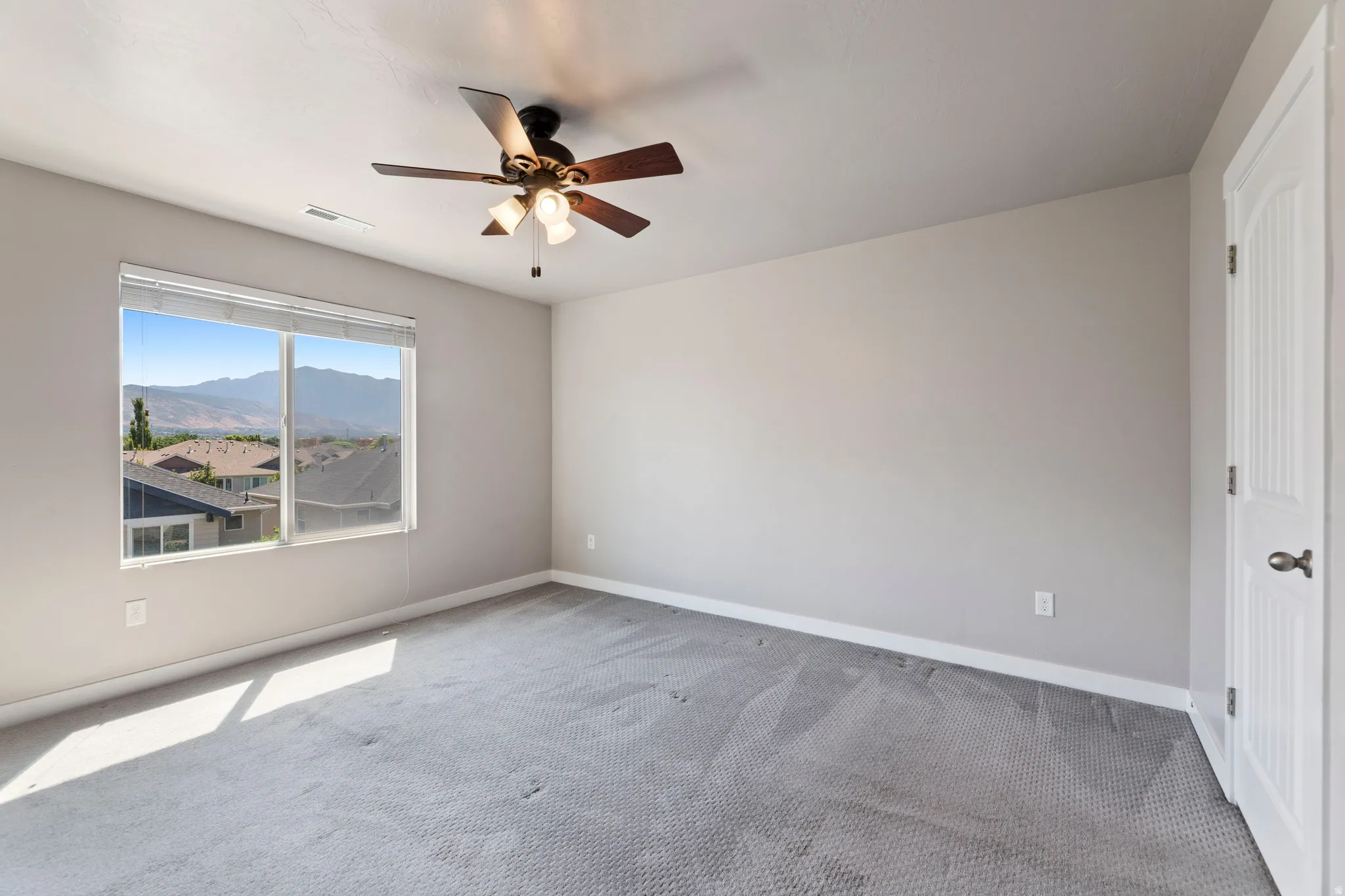 Carpeted bedroom with a ceiling fan light fixture, showcasing a large window and mountain scenery