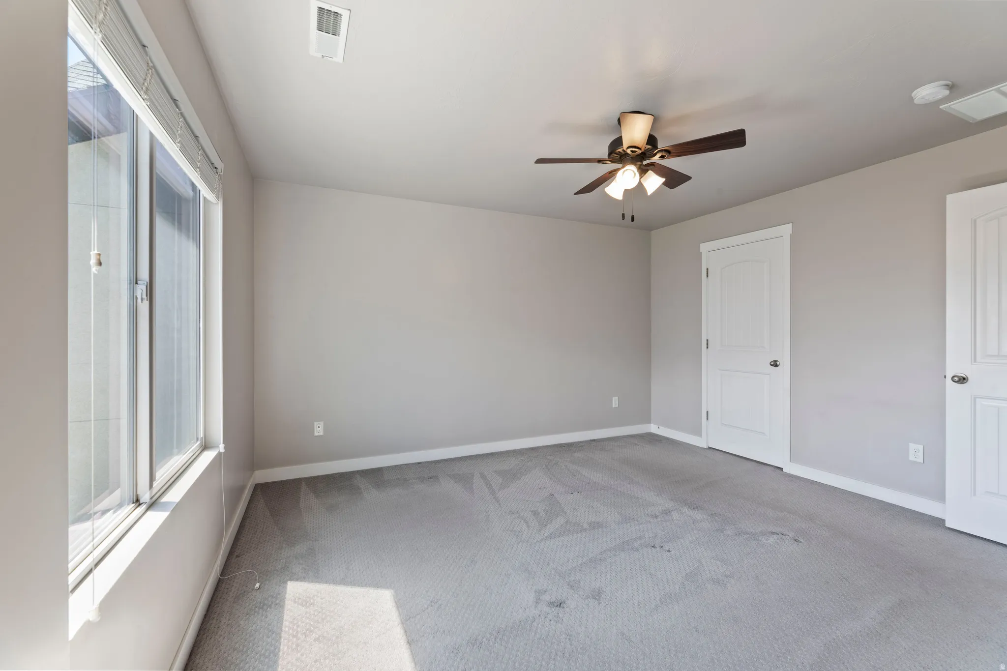 Spacious bedroom featuring light gray carpeting, a large window with blinds, and white trim