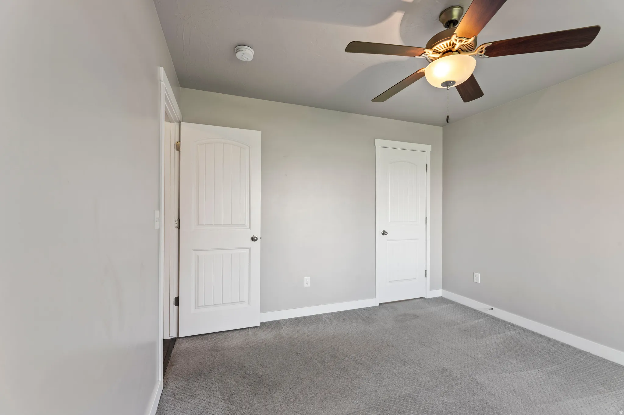 1st floor bedroom featuring a ceiling fan with integrated lighting, two paneled doors, and gray carpet flooring