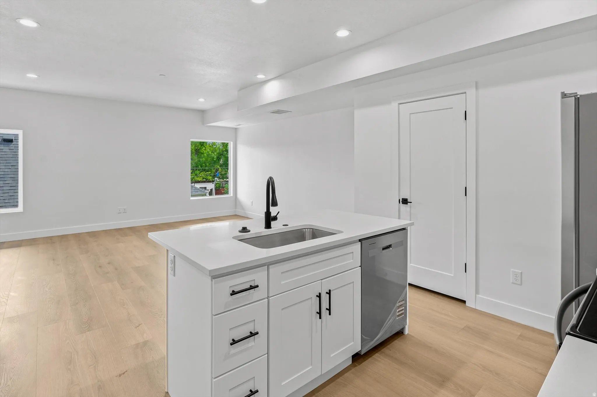 Kitchen island with white cabinetry and black hardware, featuring an undermount sink, gooseneck faucet, and integrated dishwasher