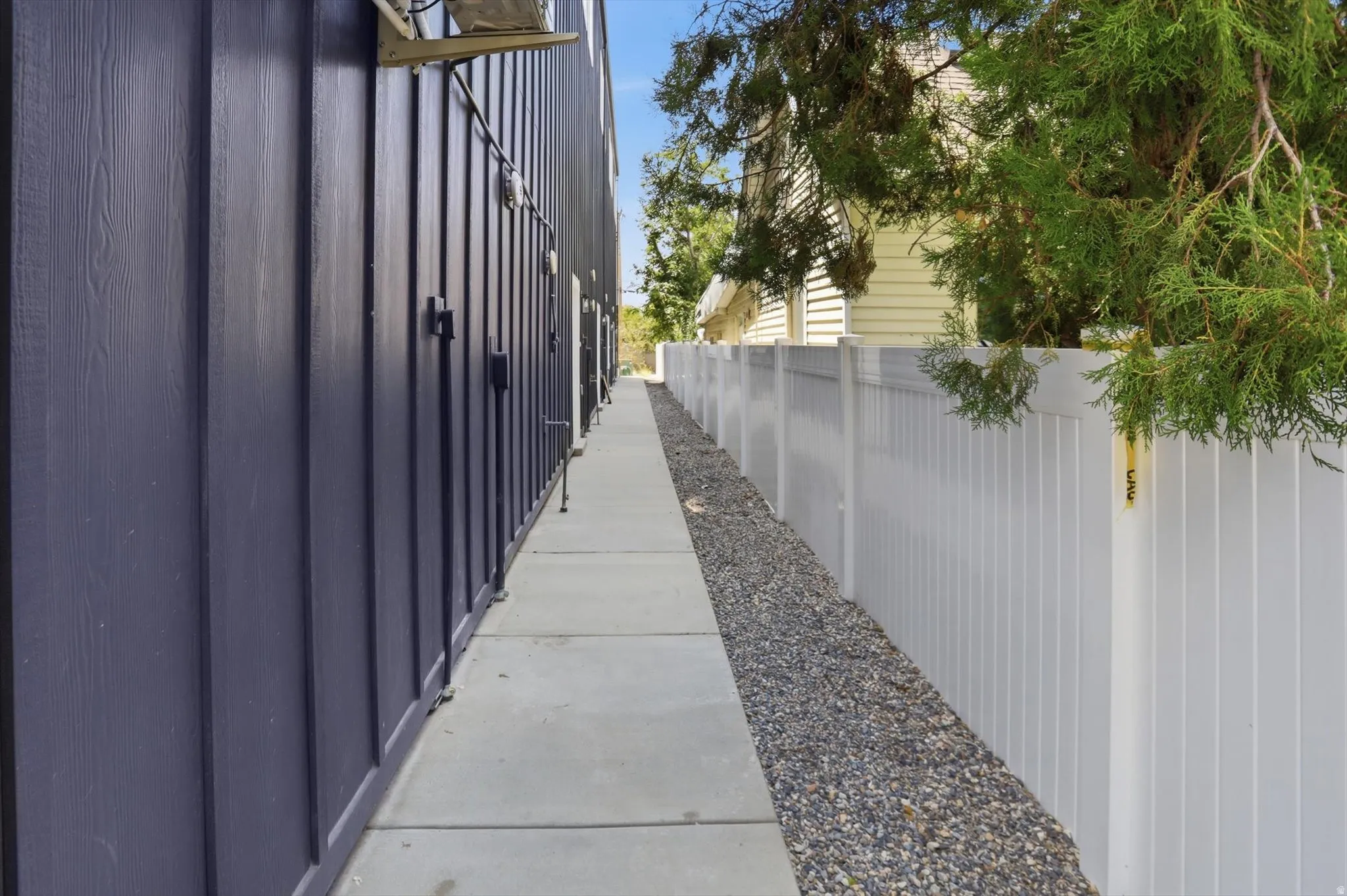 Board and batten siding on a modern exterior featuring a concrete walkway, rock landscaping, and a privacy fence