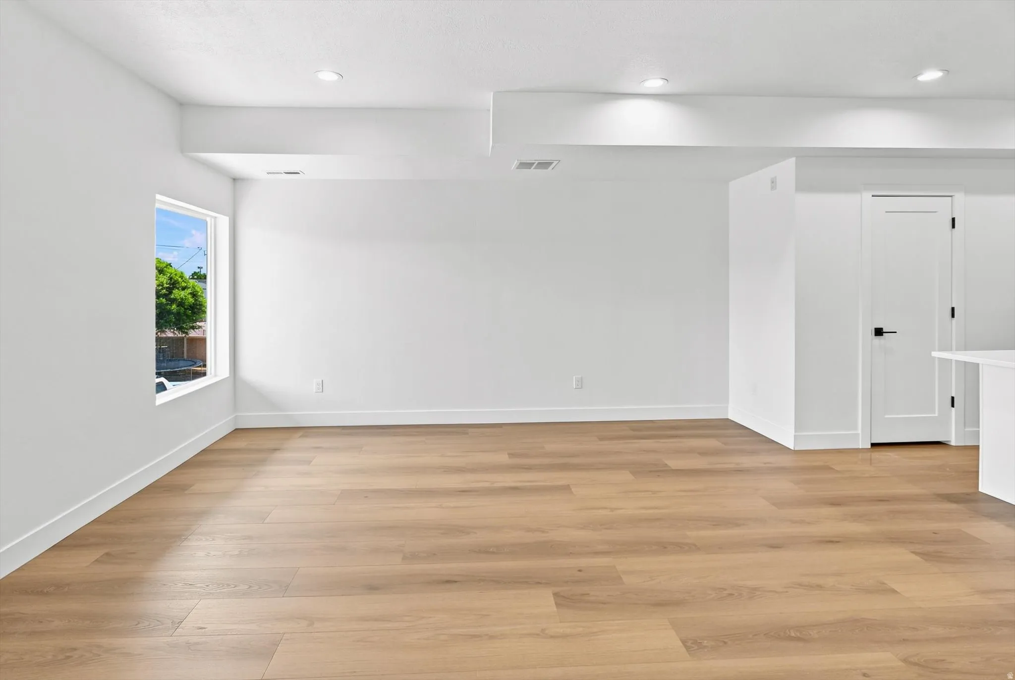 Spacious room featuring wood-finish flooring, white baseboards, and bright white walls