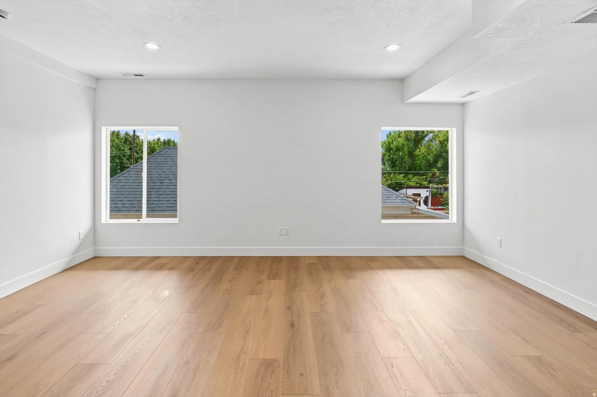 Bright room with wood-finish flooring, two windows, recessed lighting, white walls, and white trim