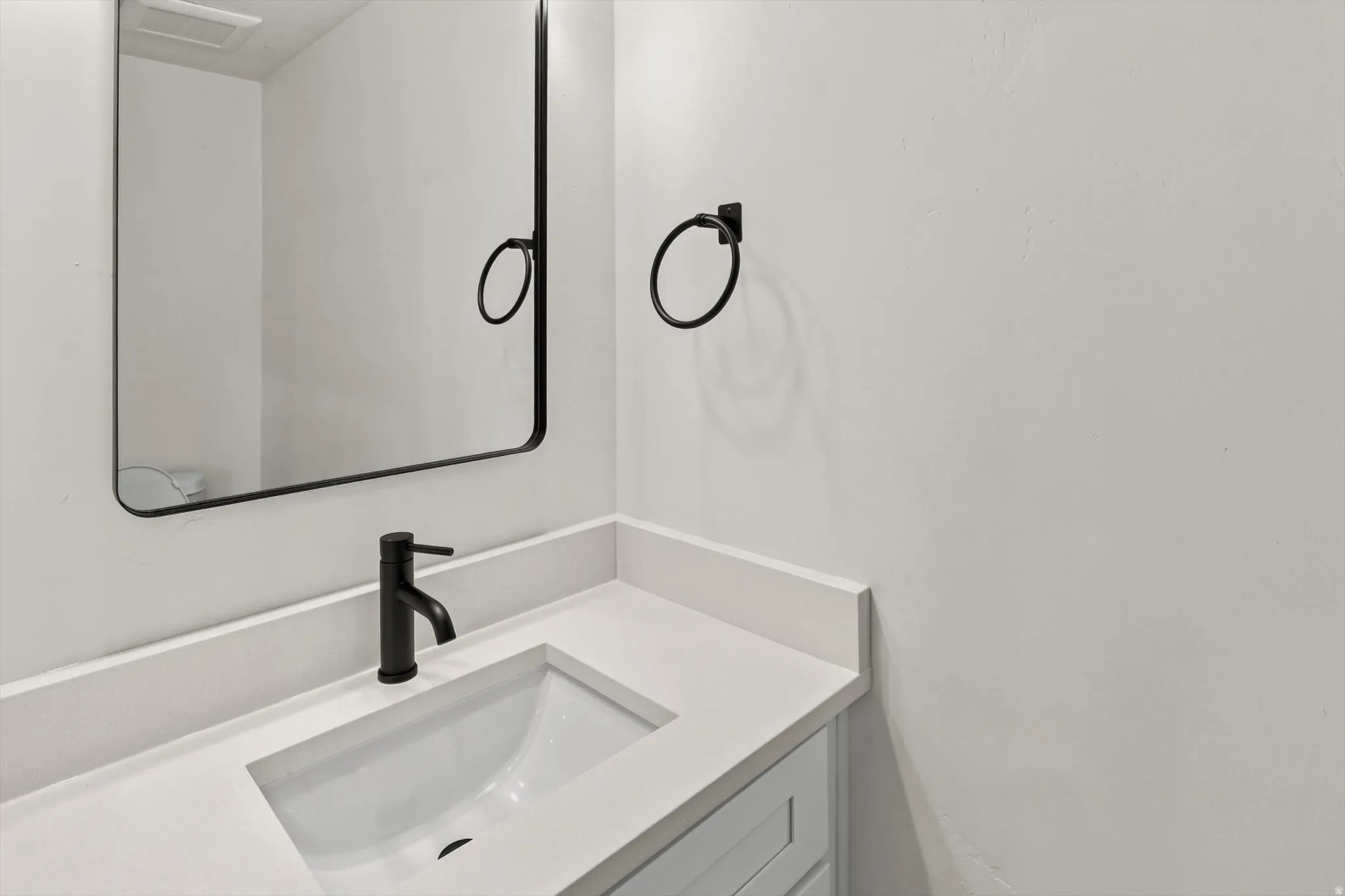 Bathroom vanity with an integrated rectangular sink, white countertop, matte black faucet, and coordinating framed mirror
