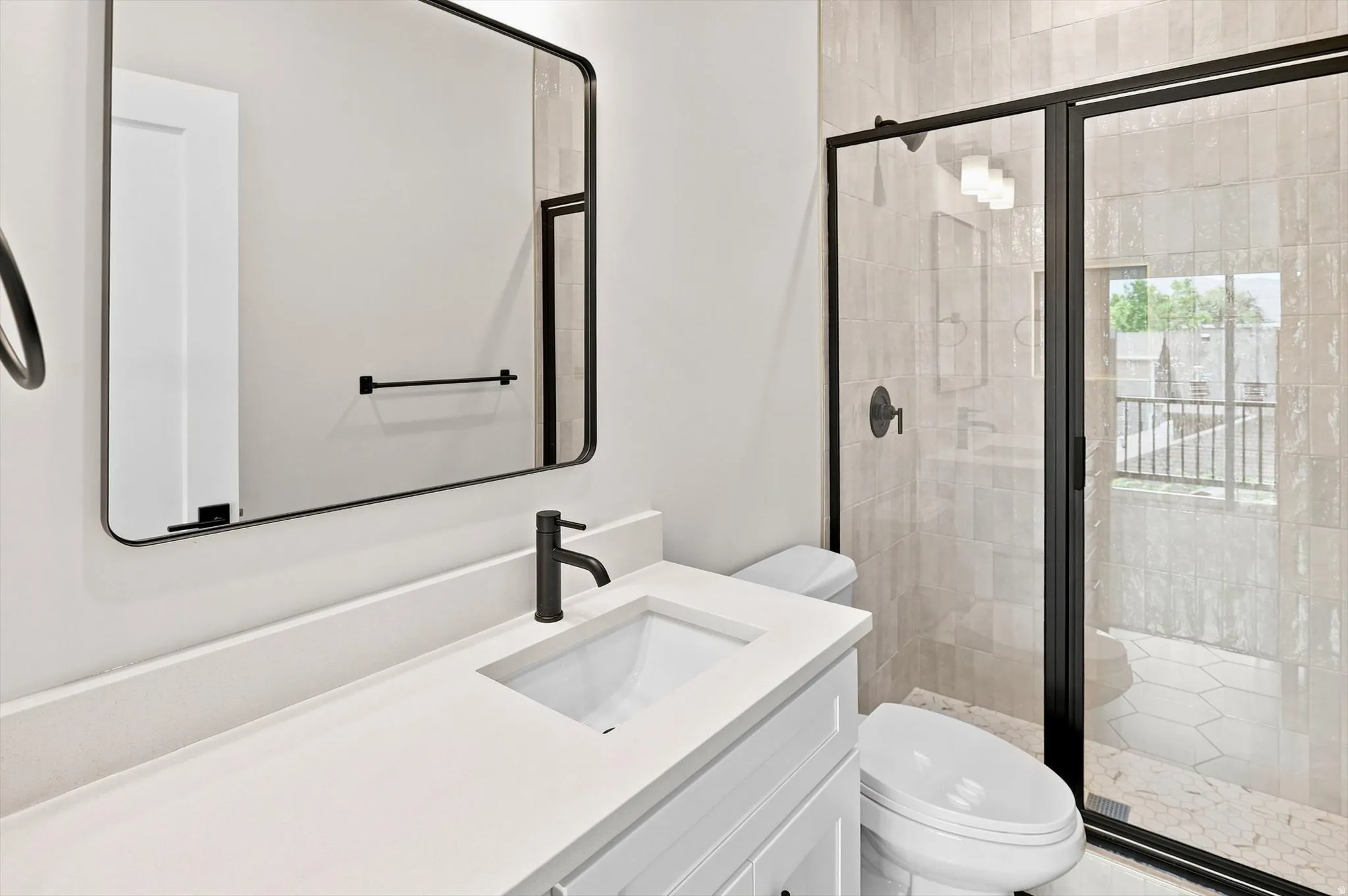 Modern bathroom featuring a single vanity with a white countertop and undermount sink, matte black faucet, and a large frameless mirror