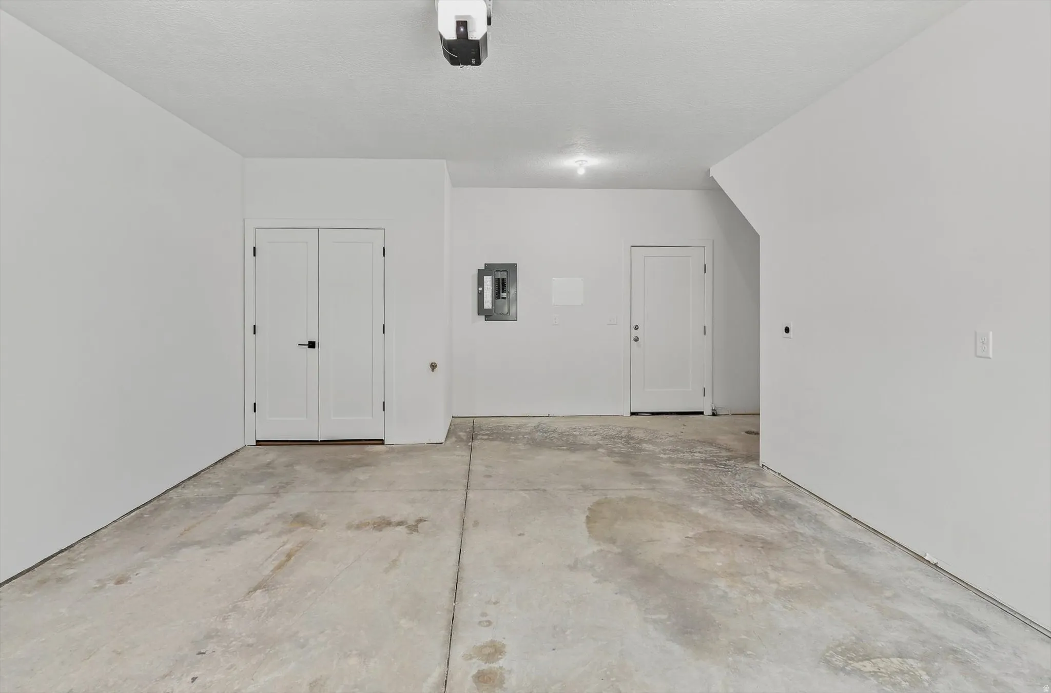 Spacious garage featuring a concrete floor, bright white walls, multiple entry points, and an overhead door opener