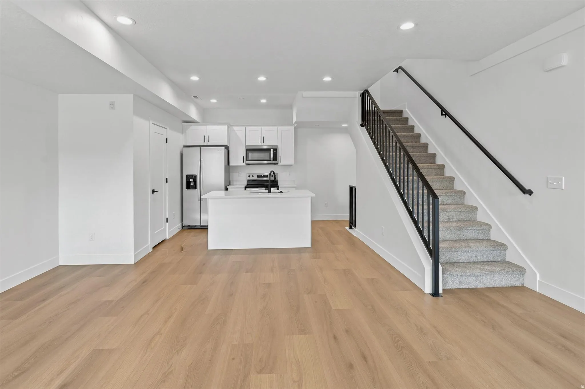 Bright open concept living space featuring wood-finish flooring, a contemporary kitchen, stainless steel appliances, white cabinetry, and recessed lighting