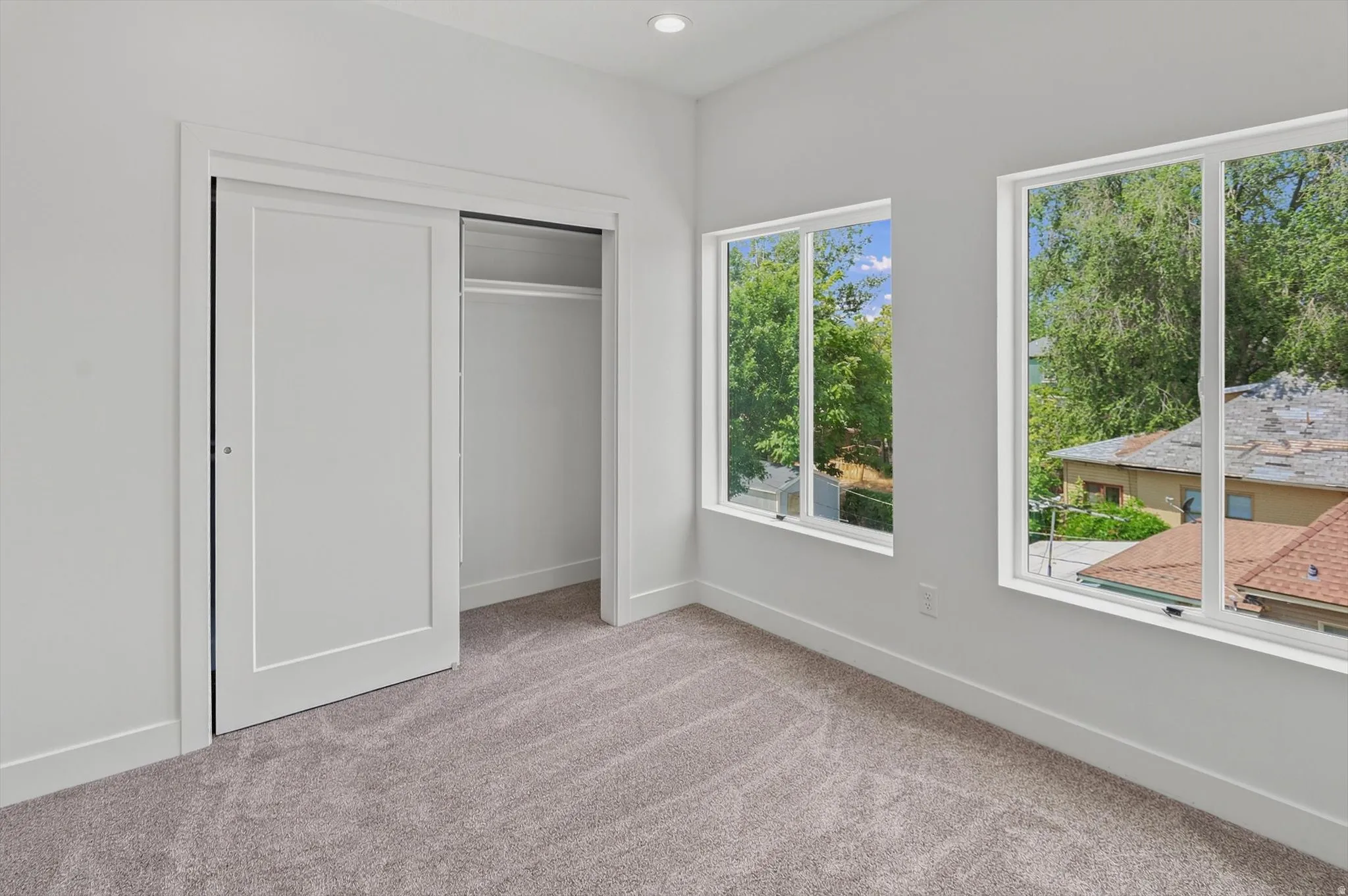 Room featuring two large windows with white frames, a sliding closet door with a white panel, light gray carpet, white baseboards, and neutral wall tones