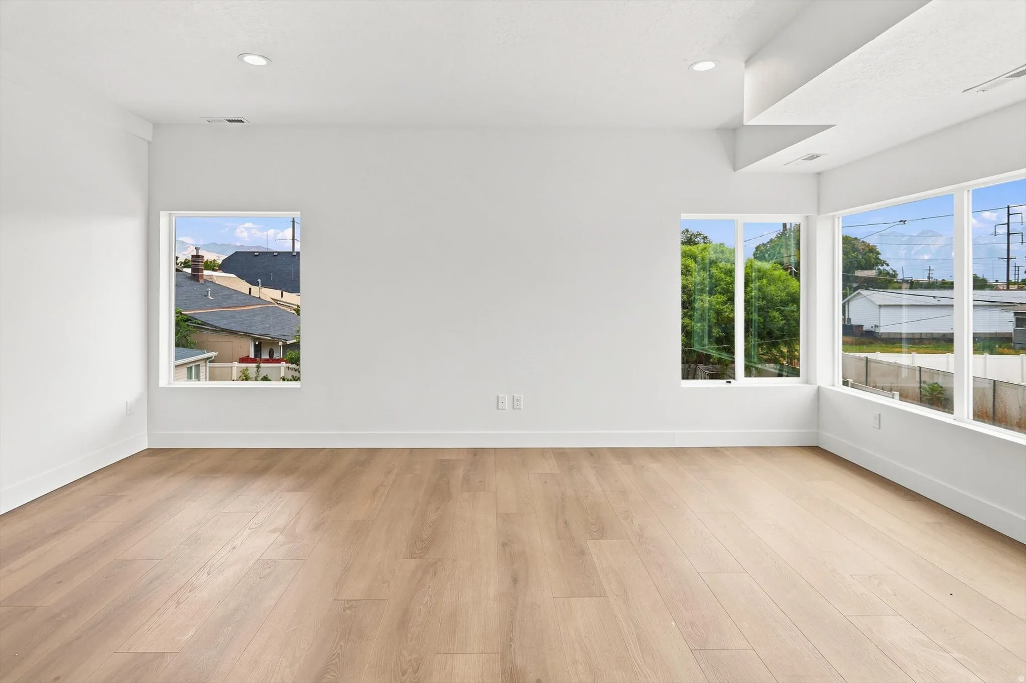 Spacious interior with light wood-finish flooring, white walls, multiple large windows, recessed ceiling lighting, and crisp white baseboards